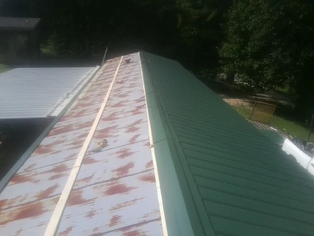 Old rusted panels beside newly installed green metal roofing — Wind Damage Roof Repair by Roofing Brothers in Conway