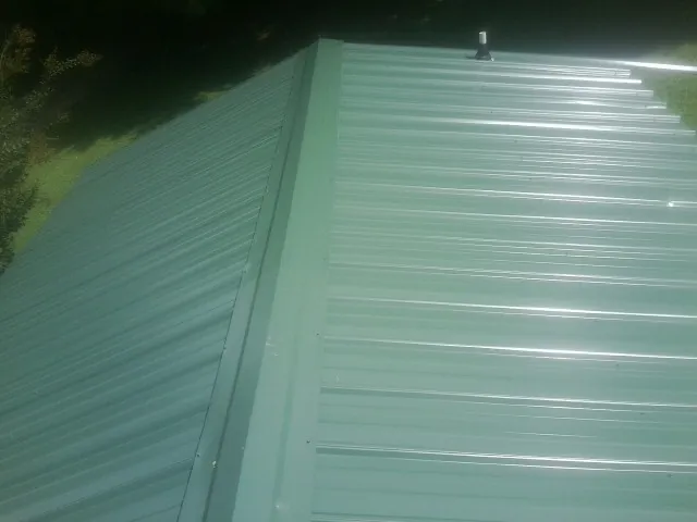 New green metal panels meeting at the ridge of a roof — Flat Roof Repair work by our crew in Conway
