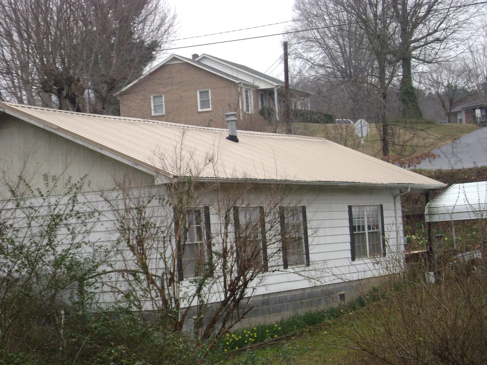 Tan metal roof on a white sided house set into a hillside — Commercial Roofing by Roofing Brothers in Conway